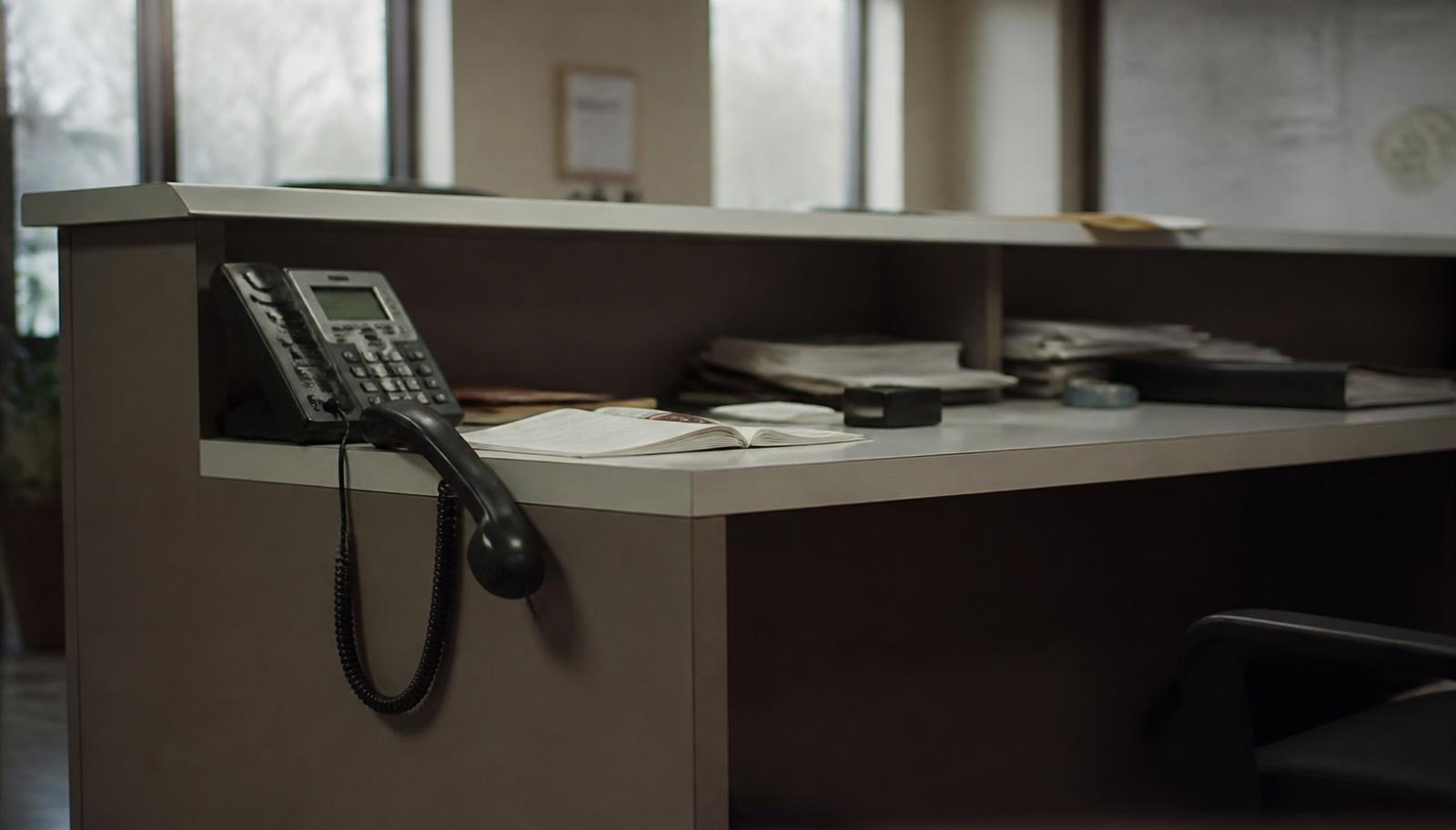 An empty reception counter with the desk phone handset left off the hook